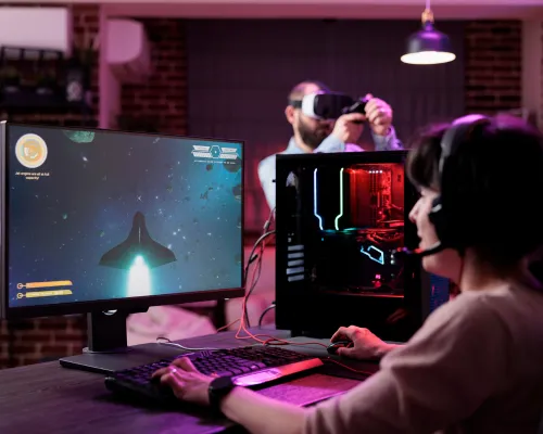 Woman testing a video game on a high-performance PC while a man uses a VR headset in the background, demonstrating how game developers use digital storytelling storyboard tools to plan gameplay, character interaction, and level design.