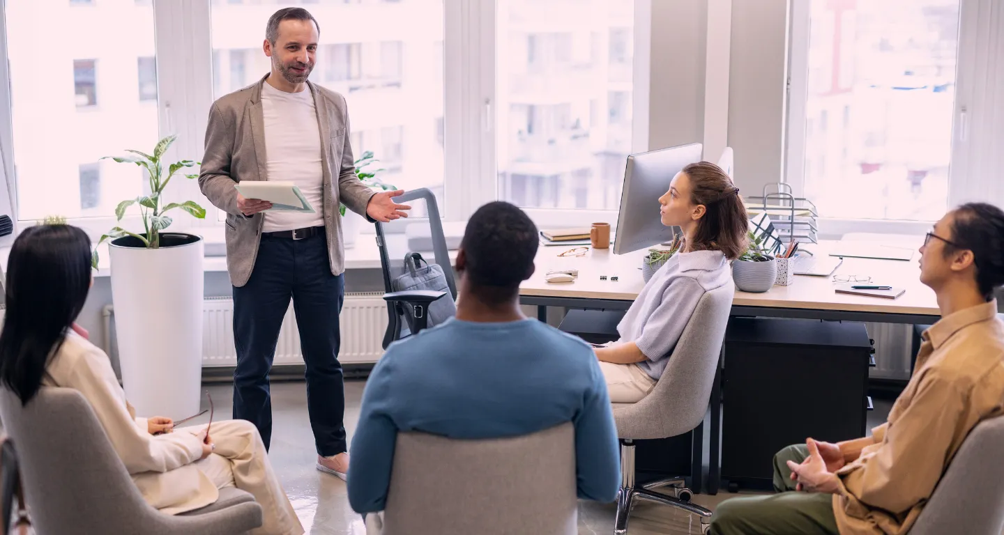 Corporate trainer addressing a seated team in a modern office, representing how businesses use a storyboarding app to create onboarding videos and internal communication modules.