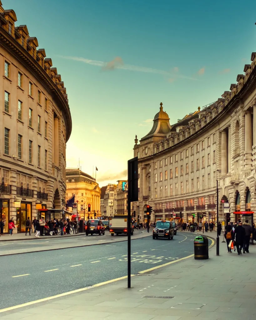 Curved street in central London with classic architecture, bustling traffic, and pedestrians at sunset, representing an ideal urban backdrop for productions using location scouting software or apps.