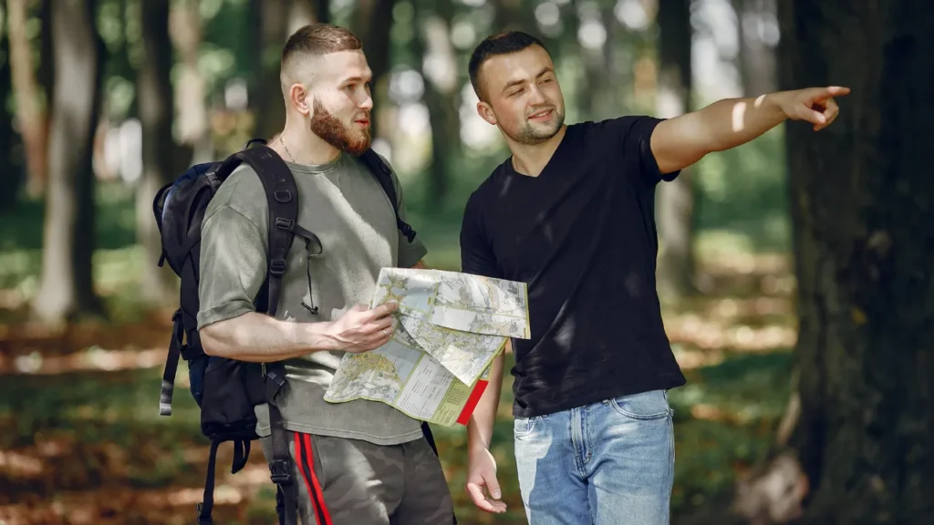 Two men in a forest holding a map and discussing directions, representing location scouting and pre-production planning costs in a film budget template, including permits, casting, and insurance.